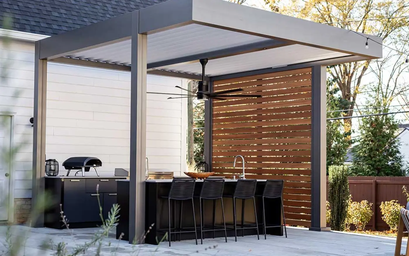Azenco louvered pergola with white roof blades covering a black outdoor kitchen and bar seating