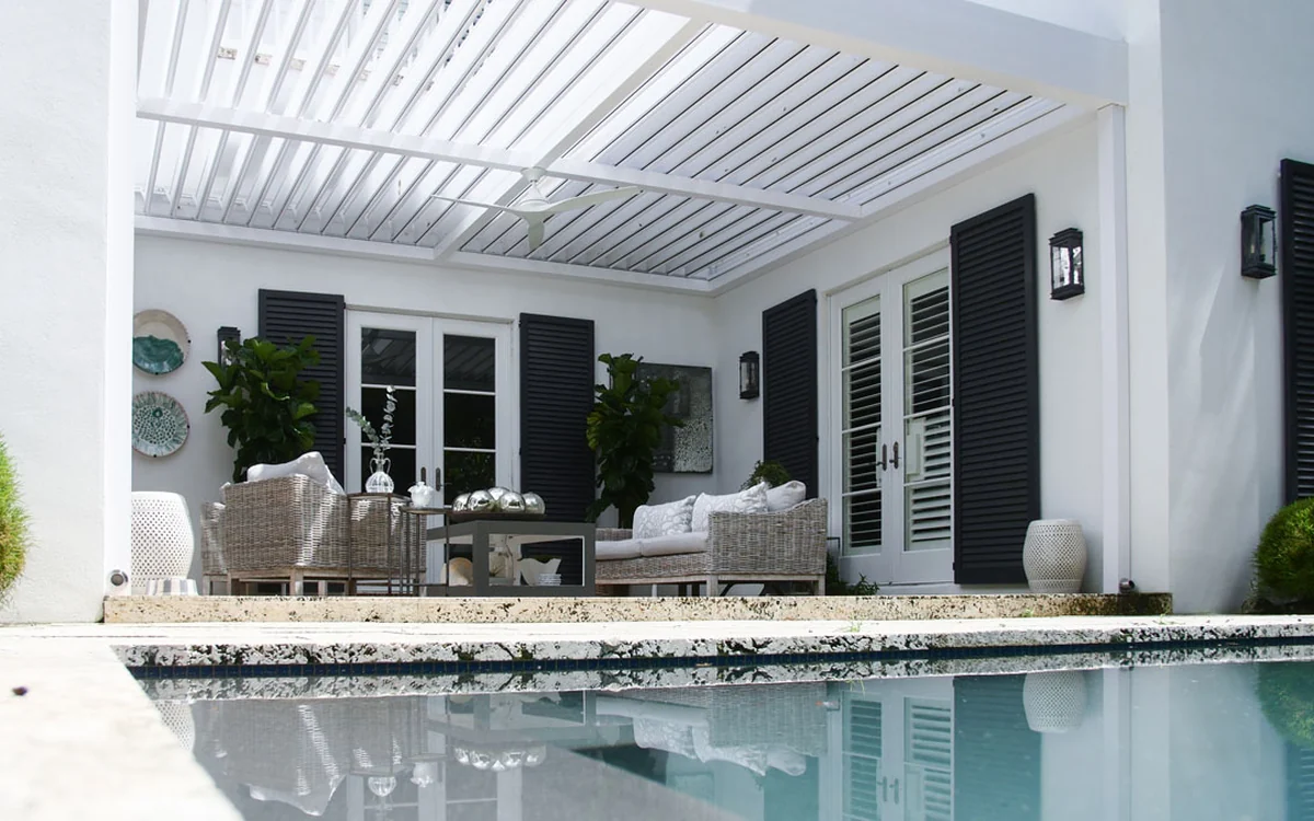 White wall-mounted Azenco R-BLADE louvered pergola integrated with a home's covered poolside patio