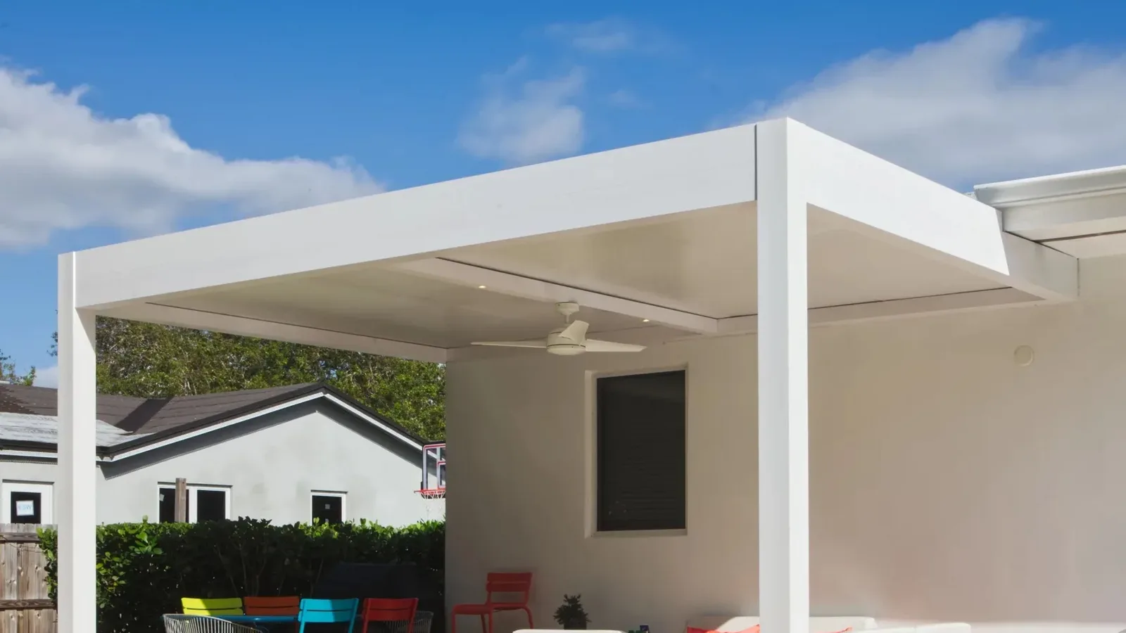 White attached solid-roof patio cover with aluminum posts beside a house