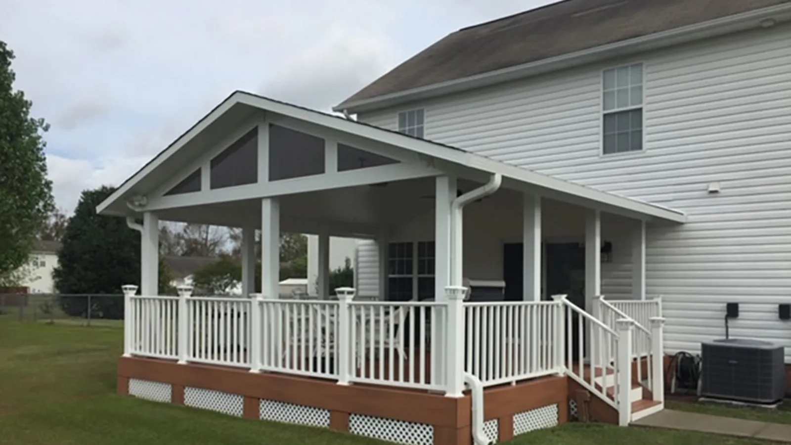 Open white attached patio cover with a gabled roof, railings, stairs, and raised deck beside a two-story home