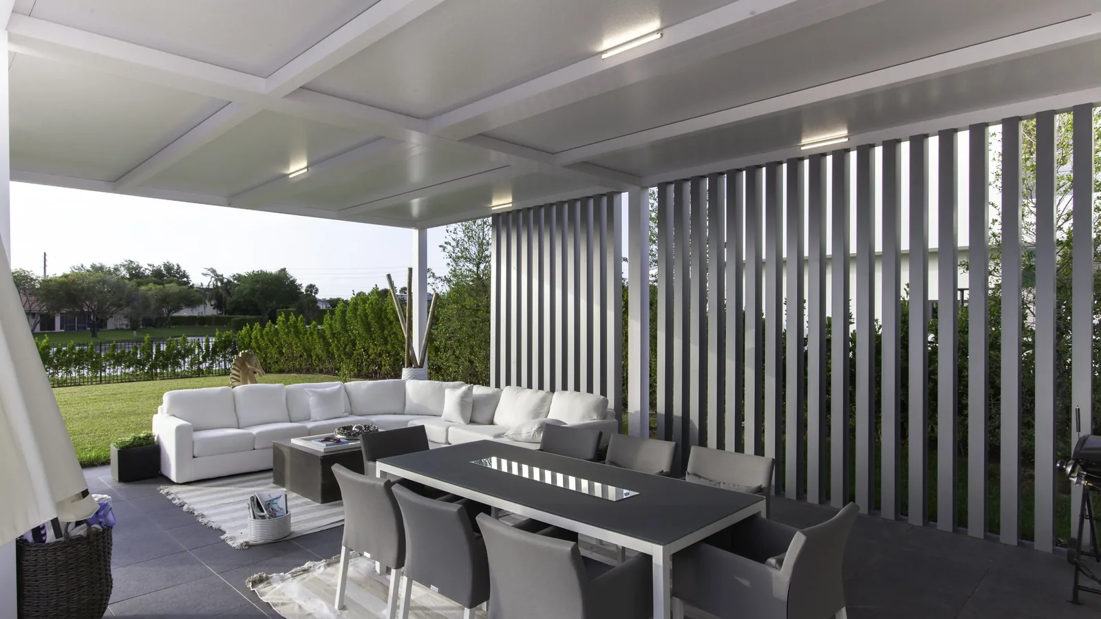 White insulated patio-cover roof above an outdoor dining and lounge area with gray privacy slats