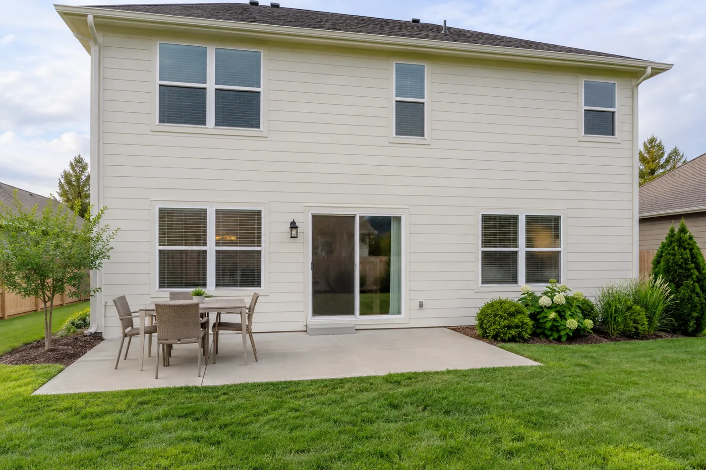 Uncovered concrete patio behind a cream siding home with outdoor seating and an open lawn