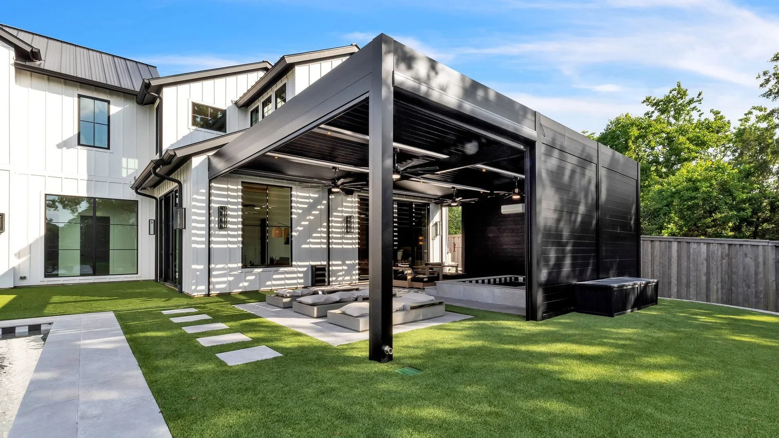 Dark aluminum louvered pergola with integrated privacy wall sections and open sides beside a modern home