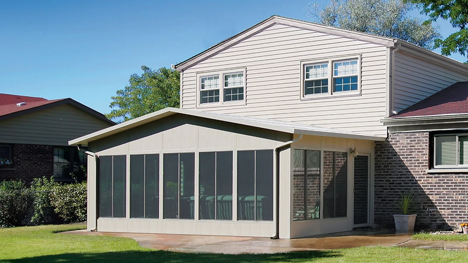 White aluminum screen room with dark mesh panels and solid lower wall panels beside a brick home