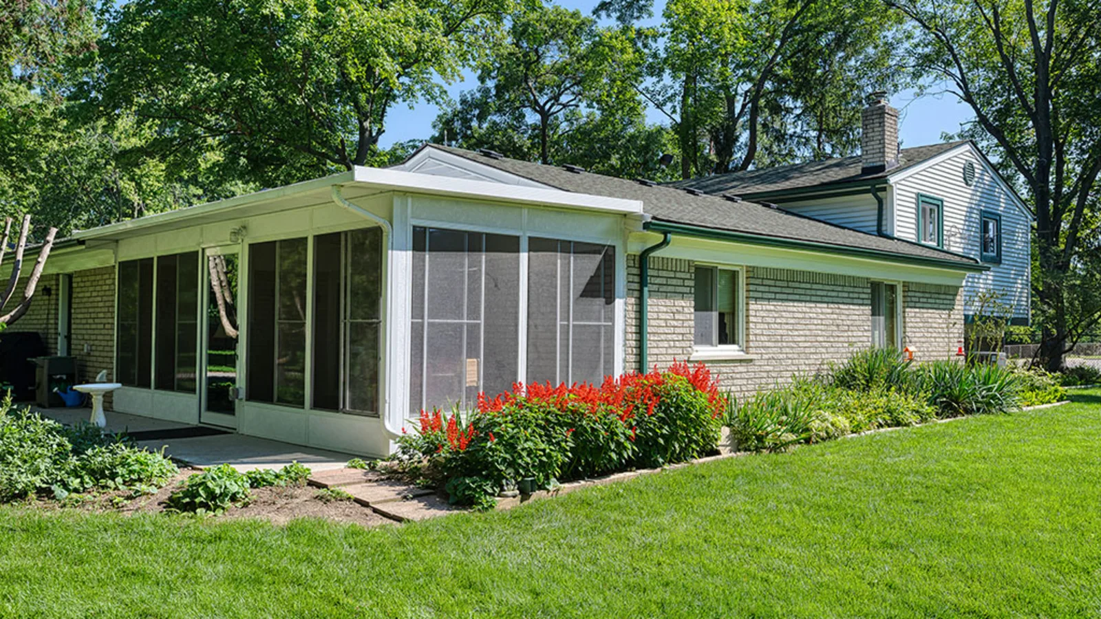 White aluminum screen room beside a narrow brick paver path and landscaped lawn